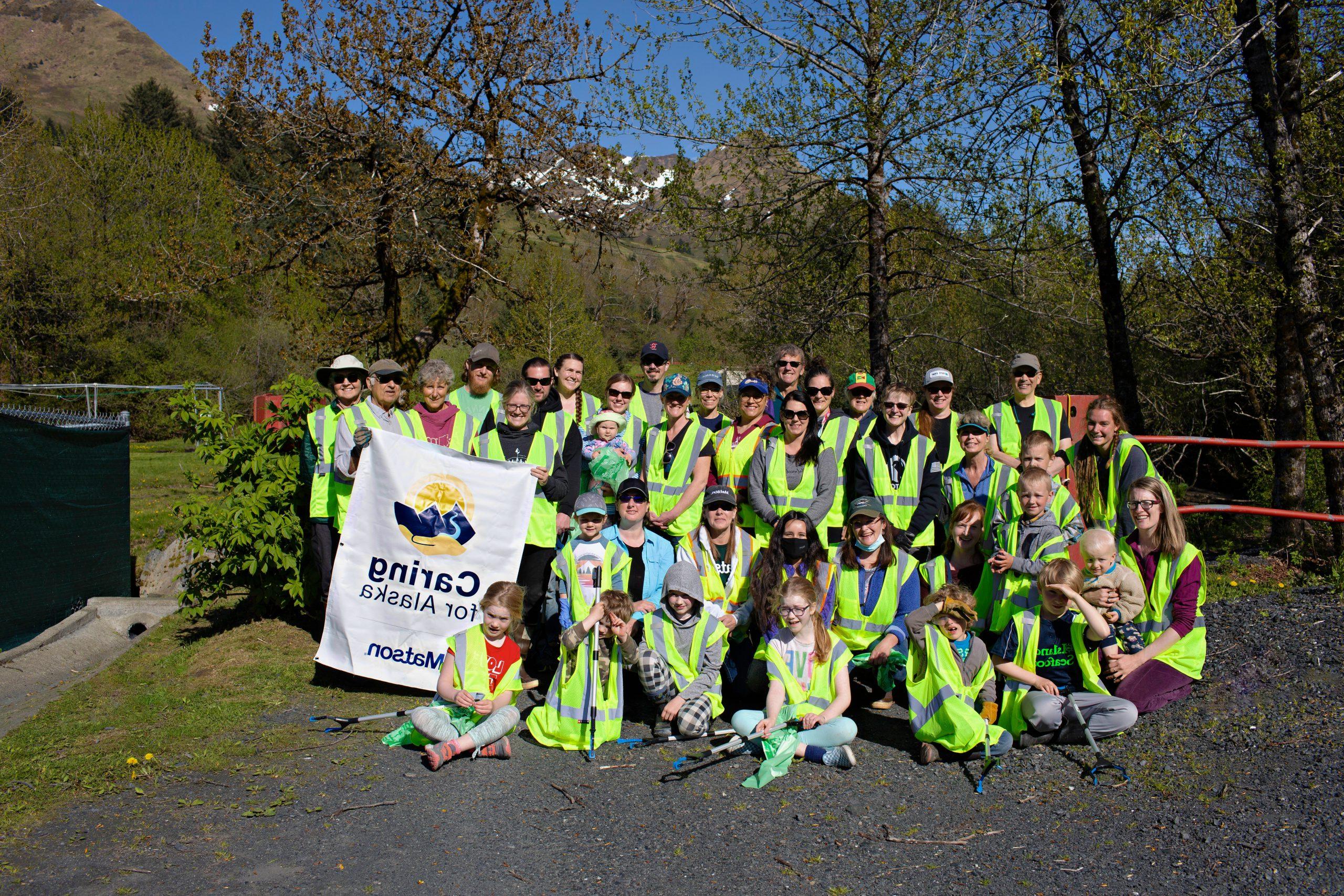 Volunteers wearing their yellow safety vests pose for a group picture with a 关爱阿拉斯加 banner.